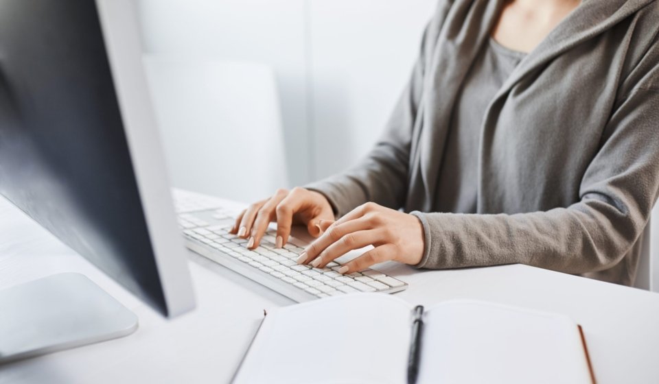 Working hard to party hard on weekends. Cropped shot of woman typing on keyboard, sitting in front of computer monitor. Freelancer translating new project, writing some notes in note pad. Office and work concept